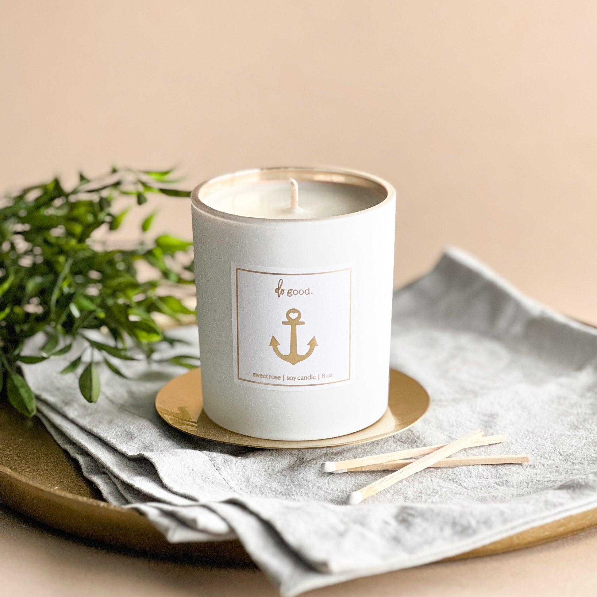 matte white candle vessel filled with soy wax and scented with "sweet rose".  label is linen white with a gold embossed anchor