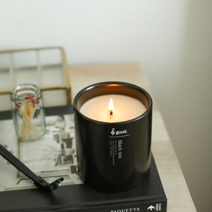 Lifestyle image of Black Sea candle on a book with a wick trimmer and matches