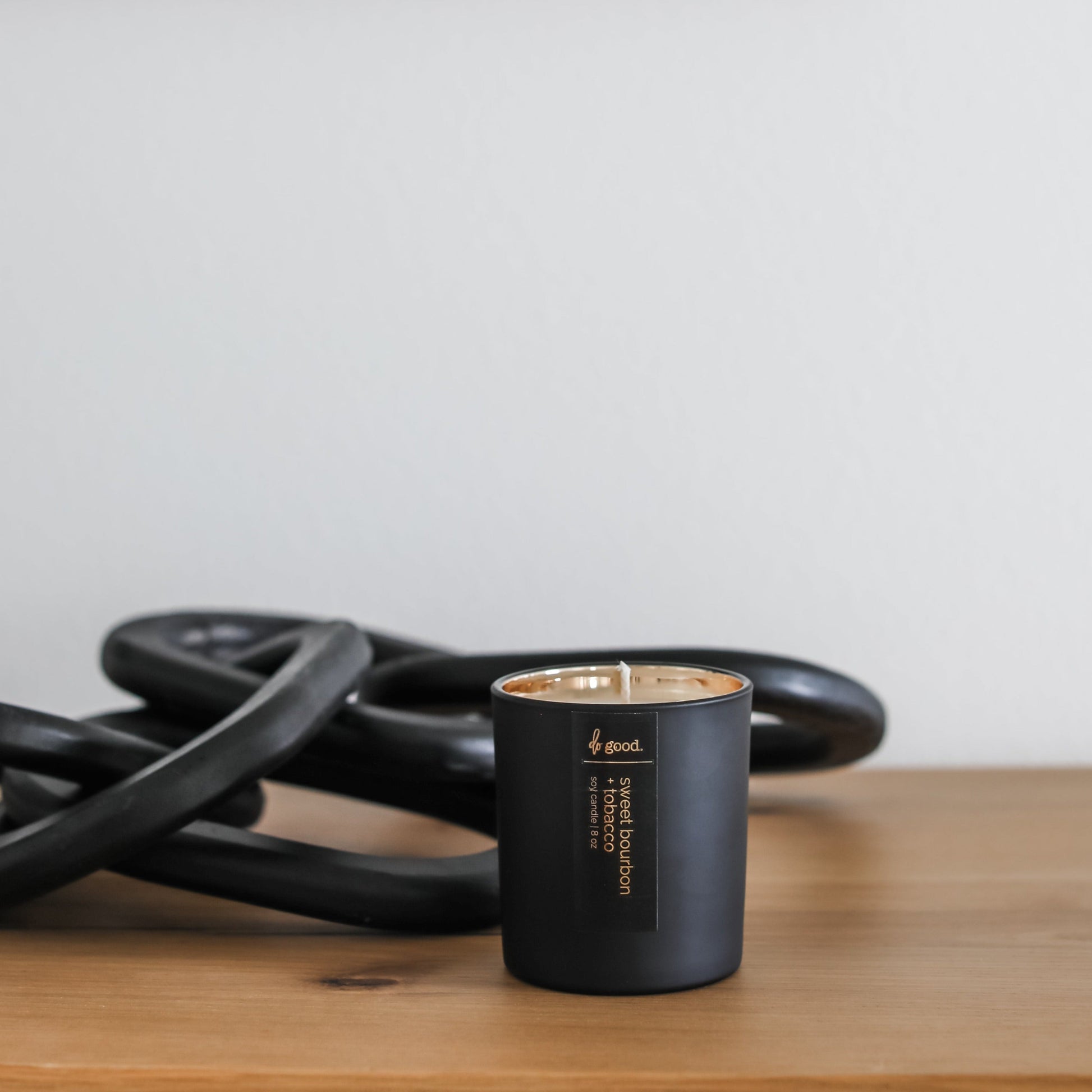 picture of a soy candle named sweet bourbon + tobacco poured into a matte black vessel with gold electroplated interior sitting on a styled console