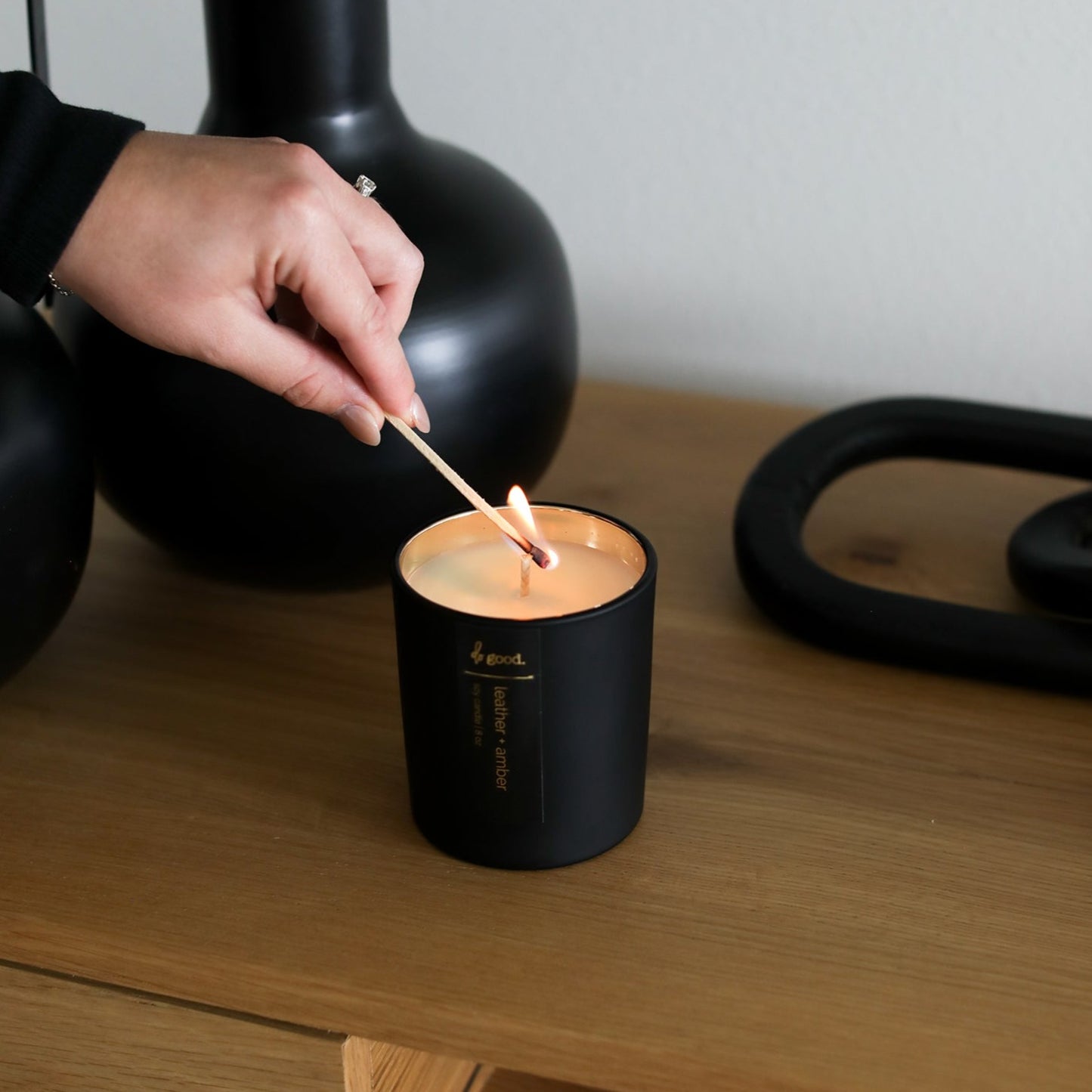 someone lighting leather and amber soy candle in a matte black vessel with electroplated interior
